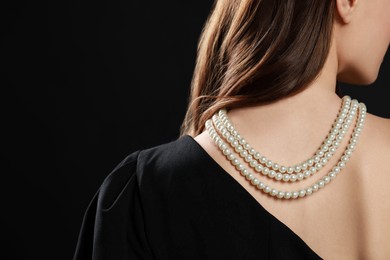 Photo of Young woman wearing elegant pearl necklace on black background, closeup. Space for text