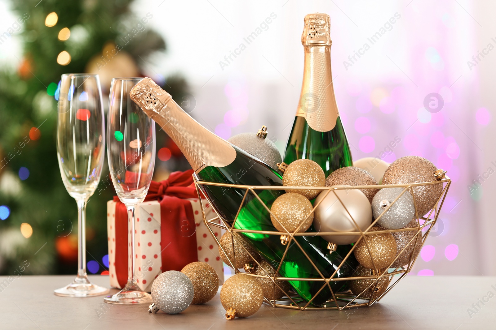 Photo of New year composition with bottles of champagne in decorative basket and blurred Christmas tree on background