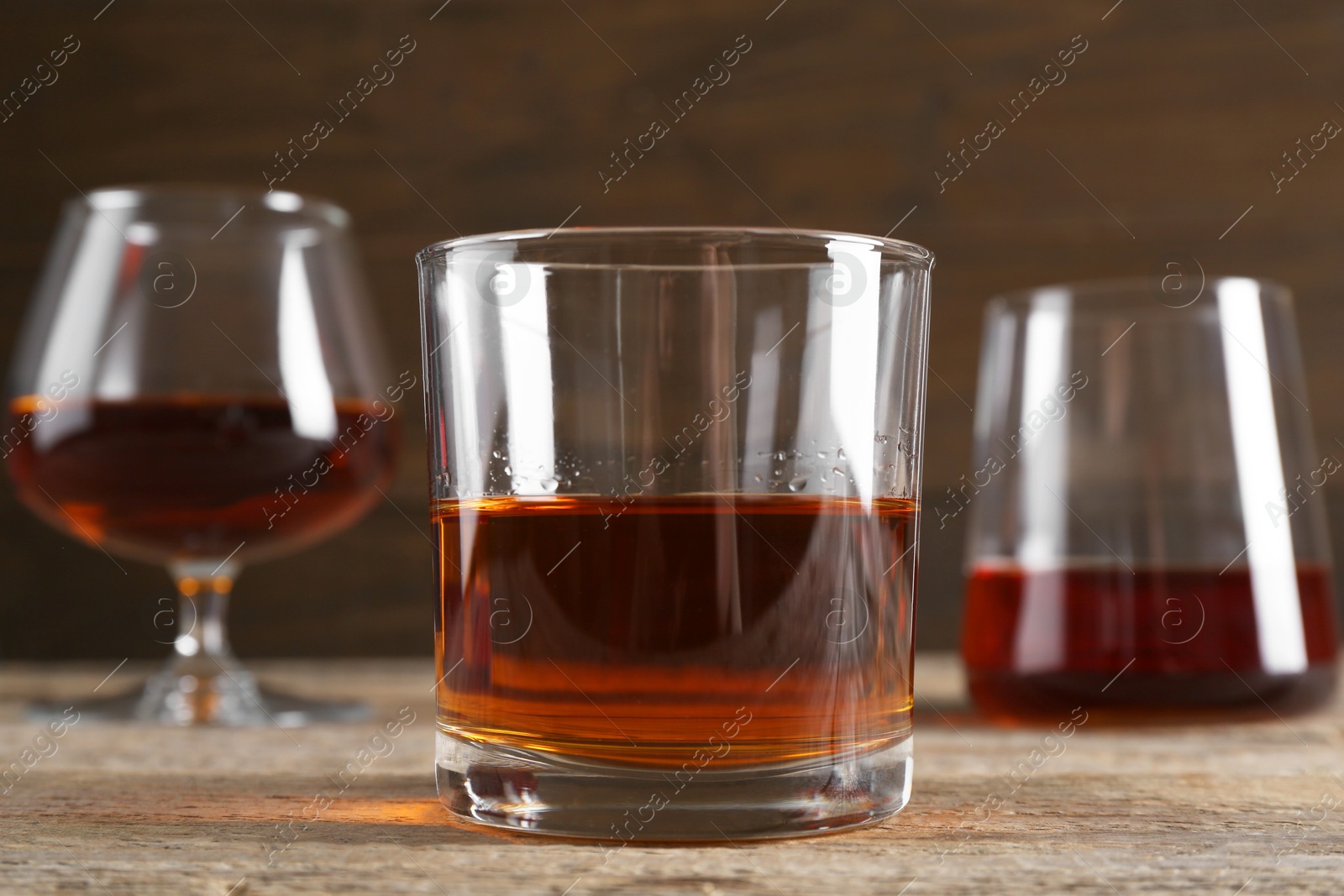 Photo of Different delicious liqueurs in glasses on wooden table