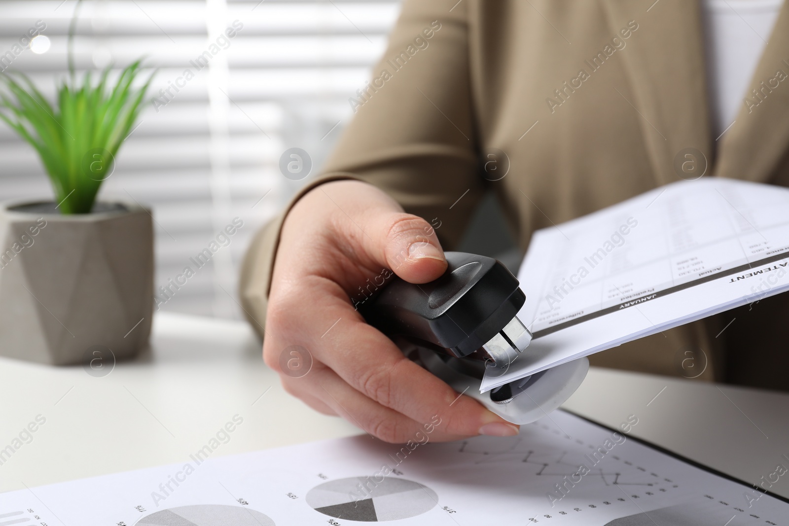 Photo of Woman with documents using stapler at white table indoors, closeup