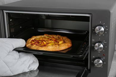 Photo of Woman taking baking pan with delicious pie from electric oven in kitchen, closeup