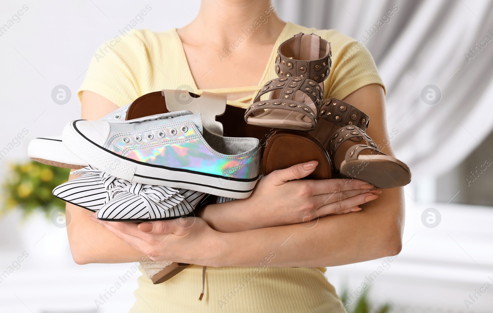 Photo of Young woman holding different shoes on blurred background, closeup