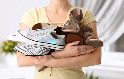 Young woman holding different shoes on blurred background, closeup