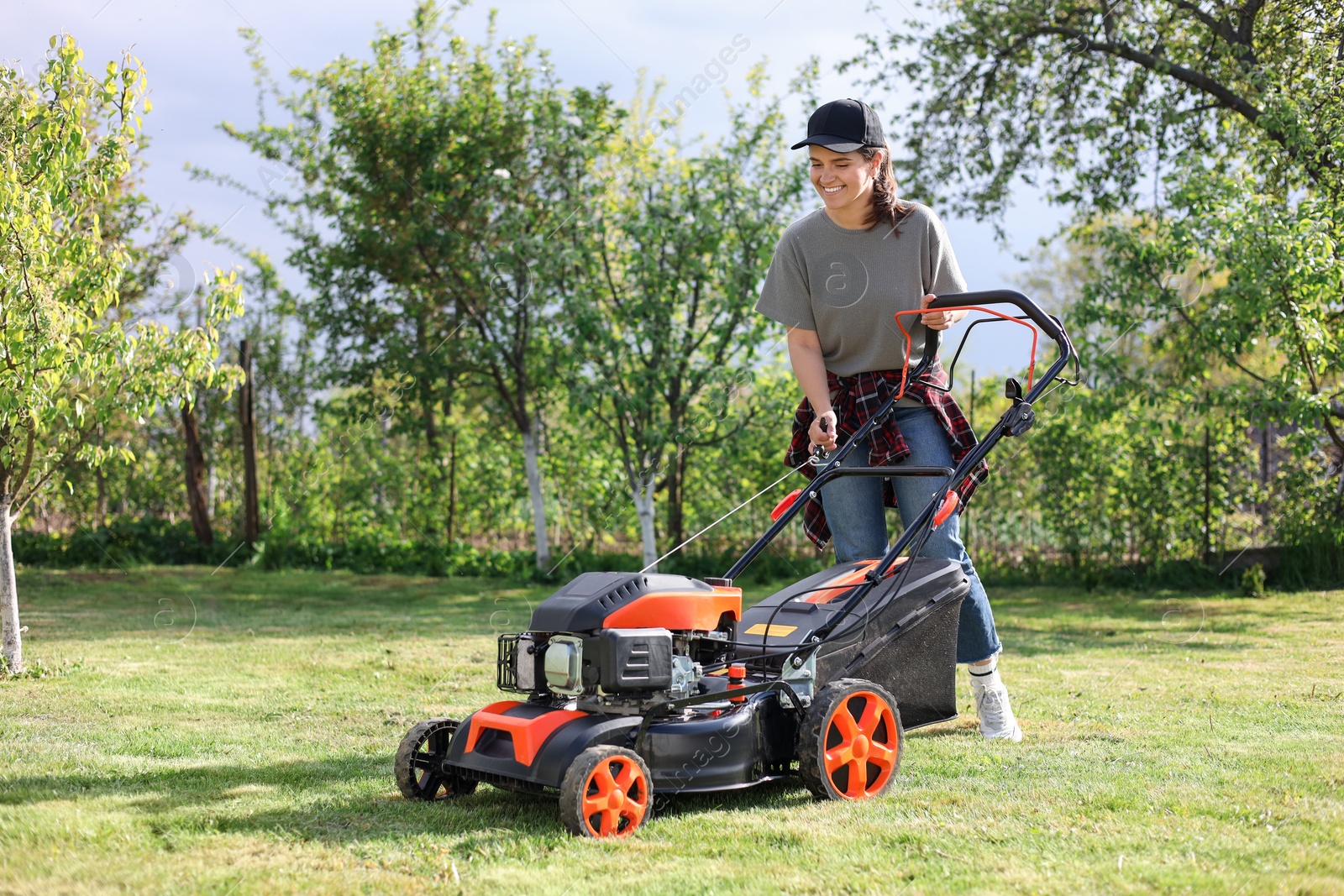 Photo of Smiling woman cutting green grass with lawn mower in garden