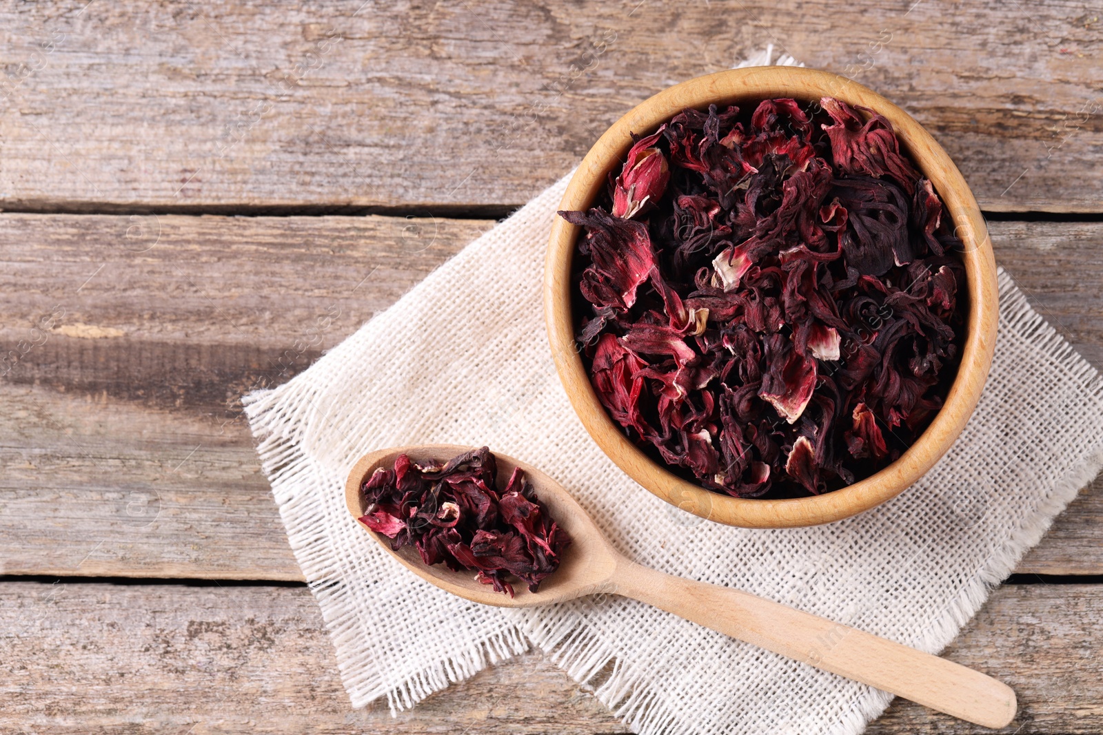 Photo of Bowl and spoon with dry hibiscus tea on wooden table, flat lay