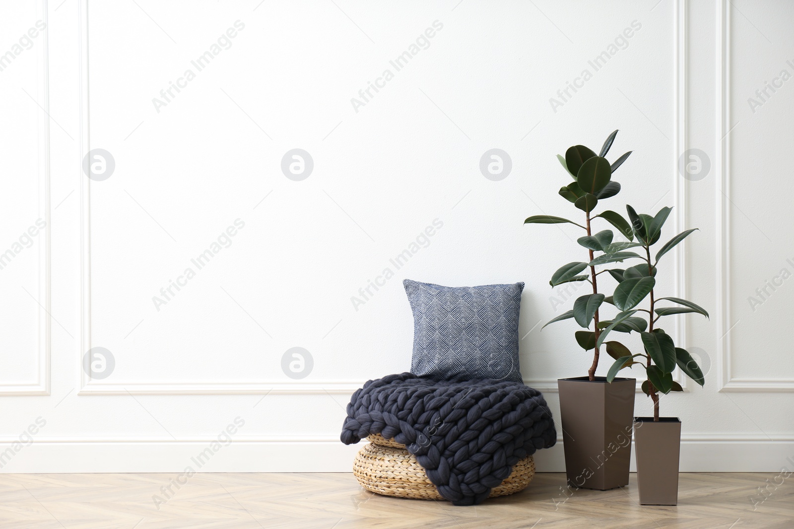 Photo of Knitted merino wool plaid and pillow on pouf in room. Space for text