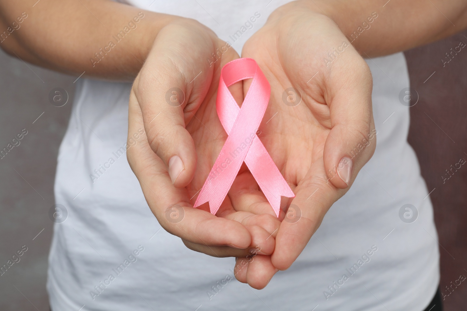 Photo of Woman holding pink ribbon on grey background, closeup. Breast cancer awareness