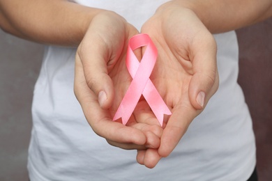 Woman holding pink ribbon on grey background, closeup. Breast cancer awareness