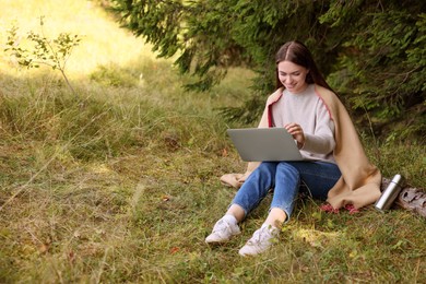 Young woman working on laptop in forest, space for text