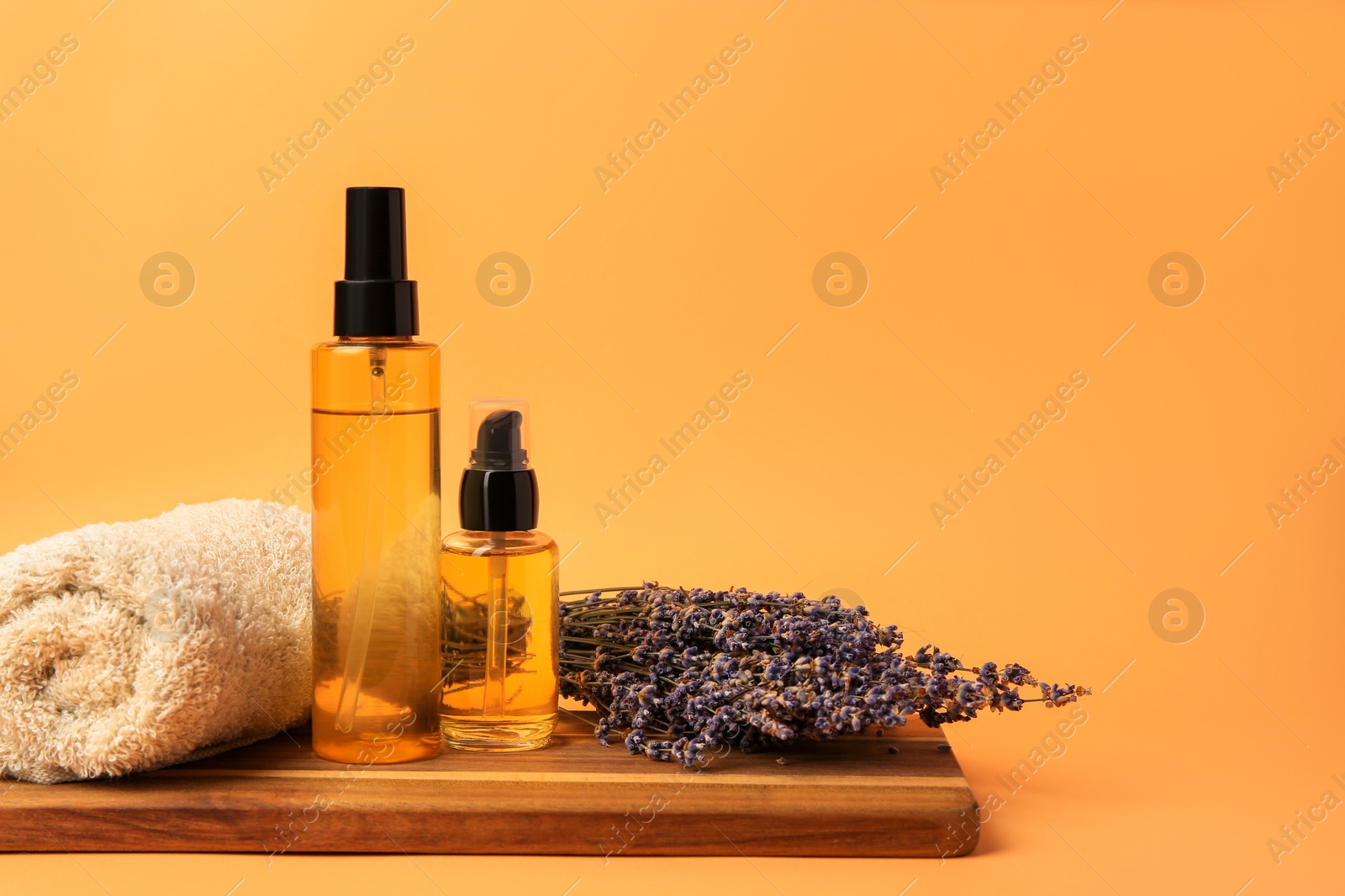 Photo of Bottles of cosmetic products, rolled towel and dry lavender flowers on orange background. Space for text