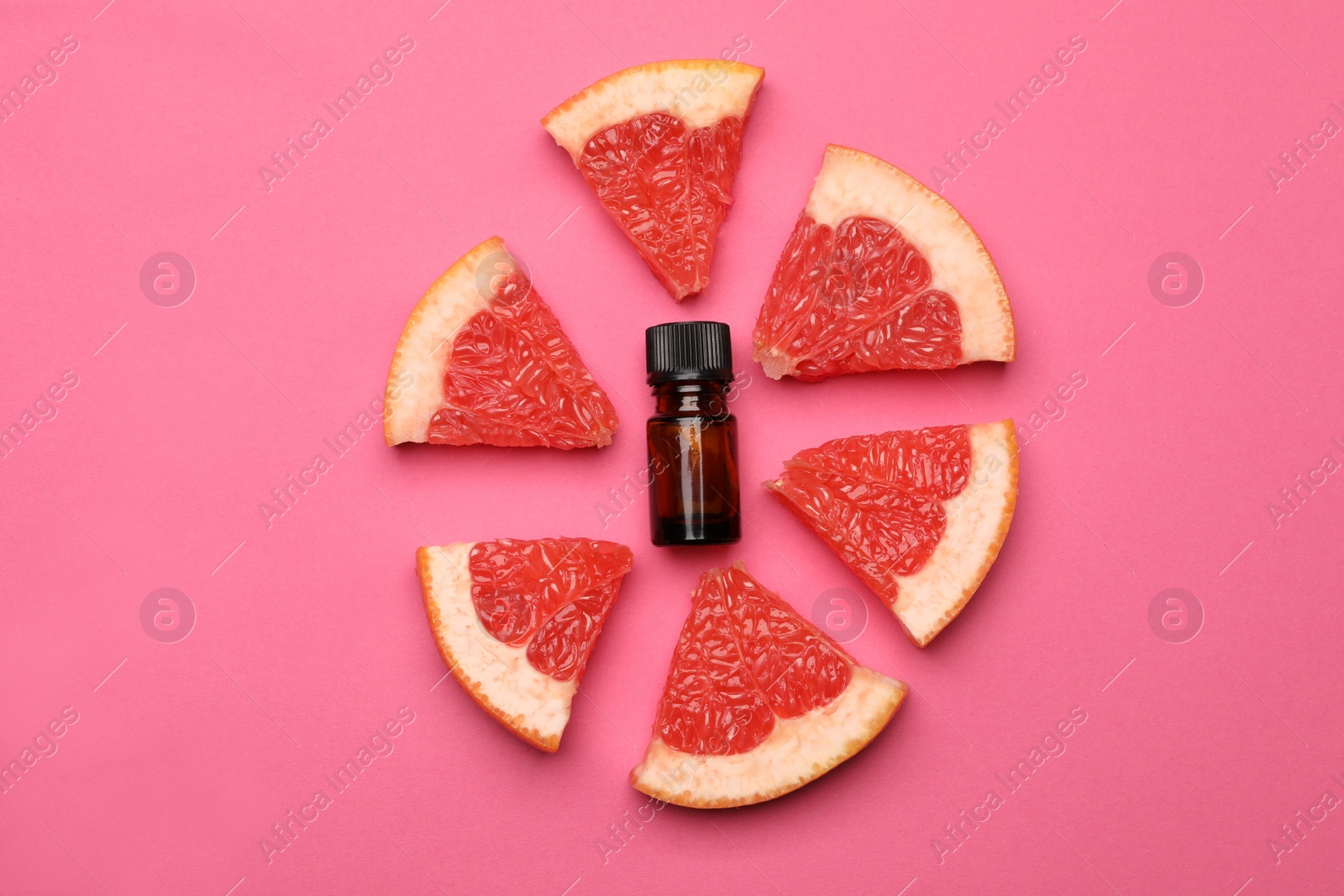 Photo of Bottle of citrus essential oil and fresh grapefruit slices on pink background, flat lay