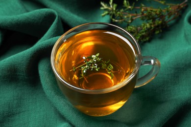 Photo of Glass cup of aromatic herbal tea with thyme on green fabric