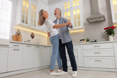 Photo of Happy affectionate senior couple dancing in kitchen, low angle view