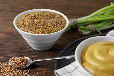 Delicious whole grain mustard, seeds and fresh green onion on wooden table, closeup