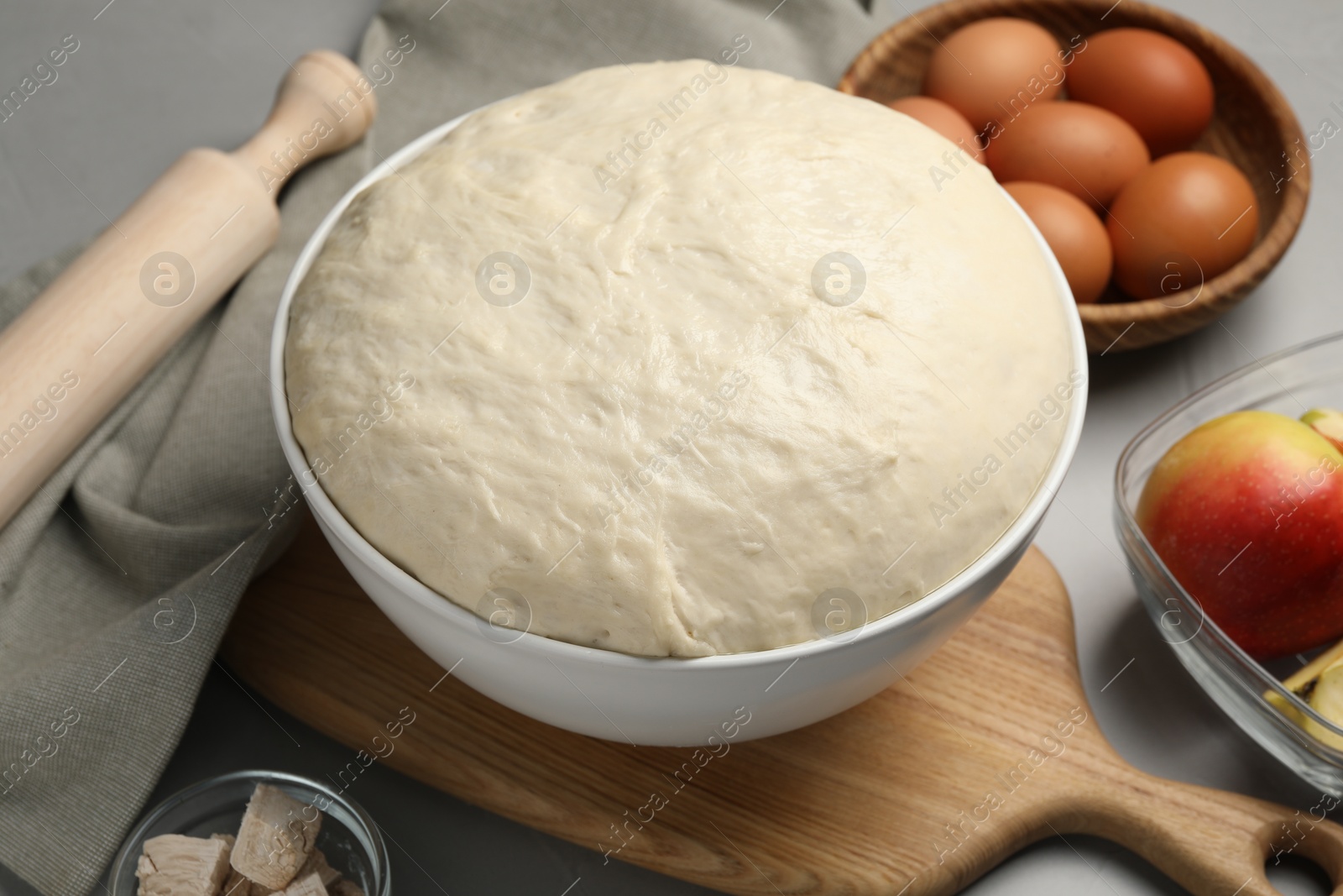 Photo of Fresh dough, rolling pin and ingredients on grey table, closeup. Cooking yeast cake