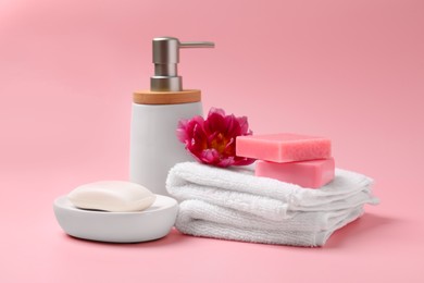 Photo of Soap bars, bottle dispenser and towels on pink background
