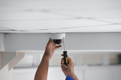 Photo of Technician installing CCTV camera on ceiling indoors, closeup