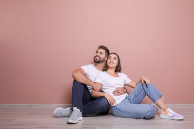 Young couple sitting on floor near pink wall indoors