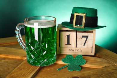 Photo of St. Patrick's day celebrating on March 17. Green beer, block calendar, leprechaun hat and decorative clover leaf on wooden table