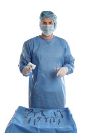 Doctor holding medical clamps with pad near table of different surgical instruments on light background