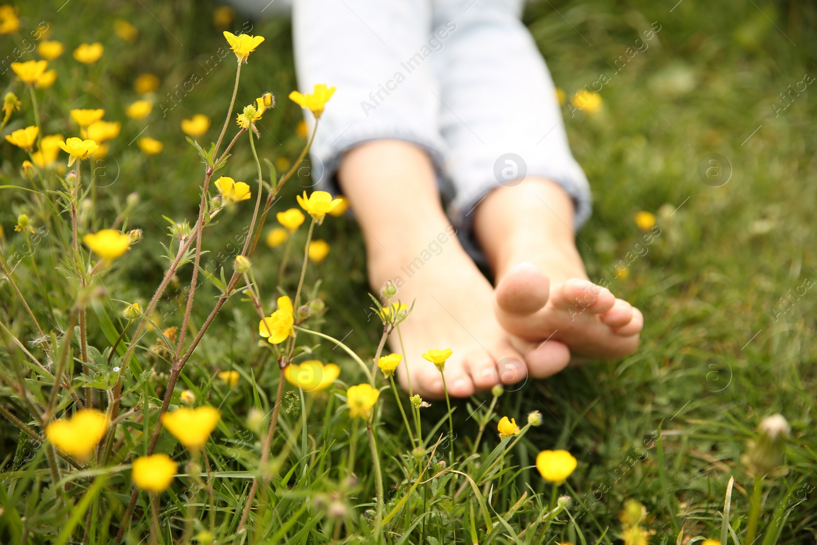 Photo of Woman sitting barefoot on green grass outdoors, closeup