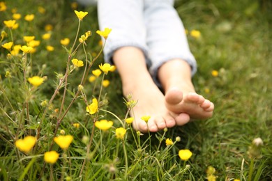 Woman sitting barefoot on green grass outdoors, closeup