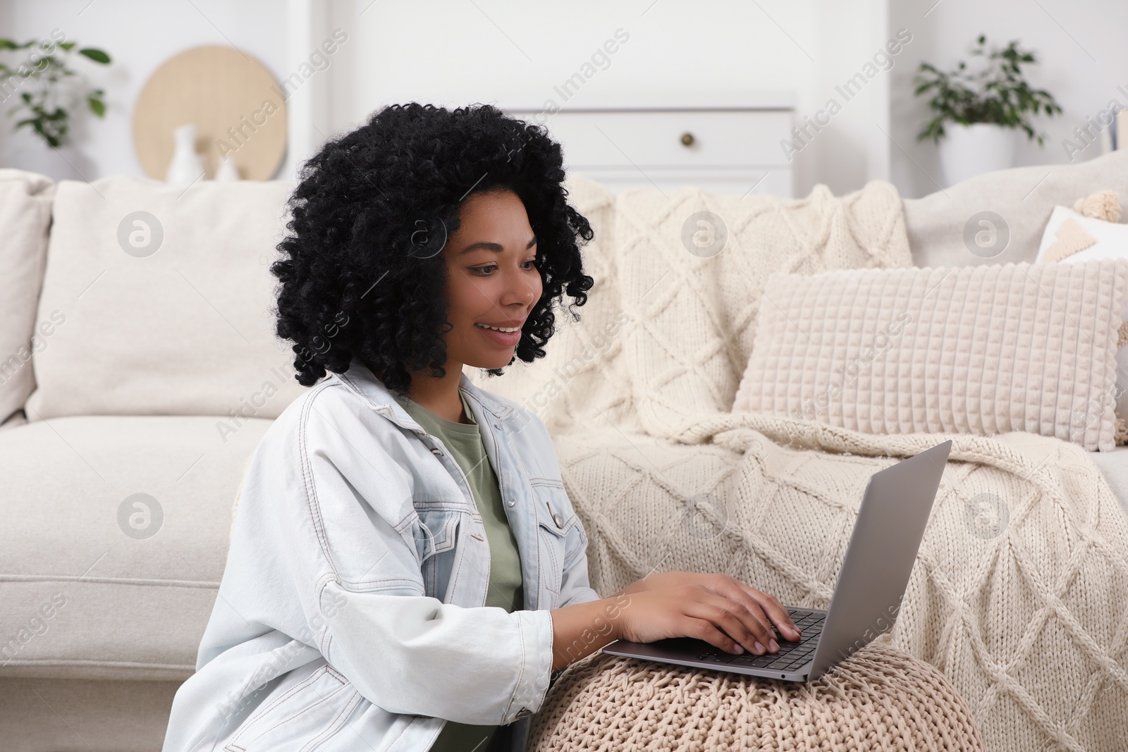 Photo of Happy young woman using laptop on pouf at home