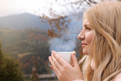 Young woman with cup of hot drink in mountains. Space for text