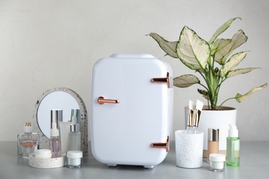 Photo of Cosmetic refrigerator and skin care products on beige background