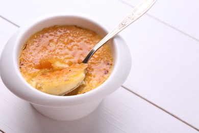 Delicious creme brulee in bowl served on white wooden table, closeup