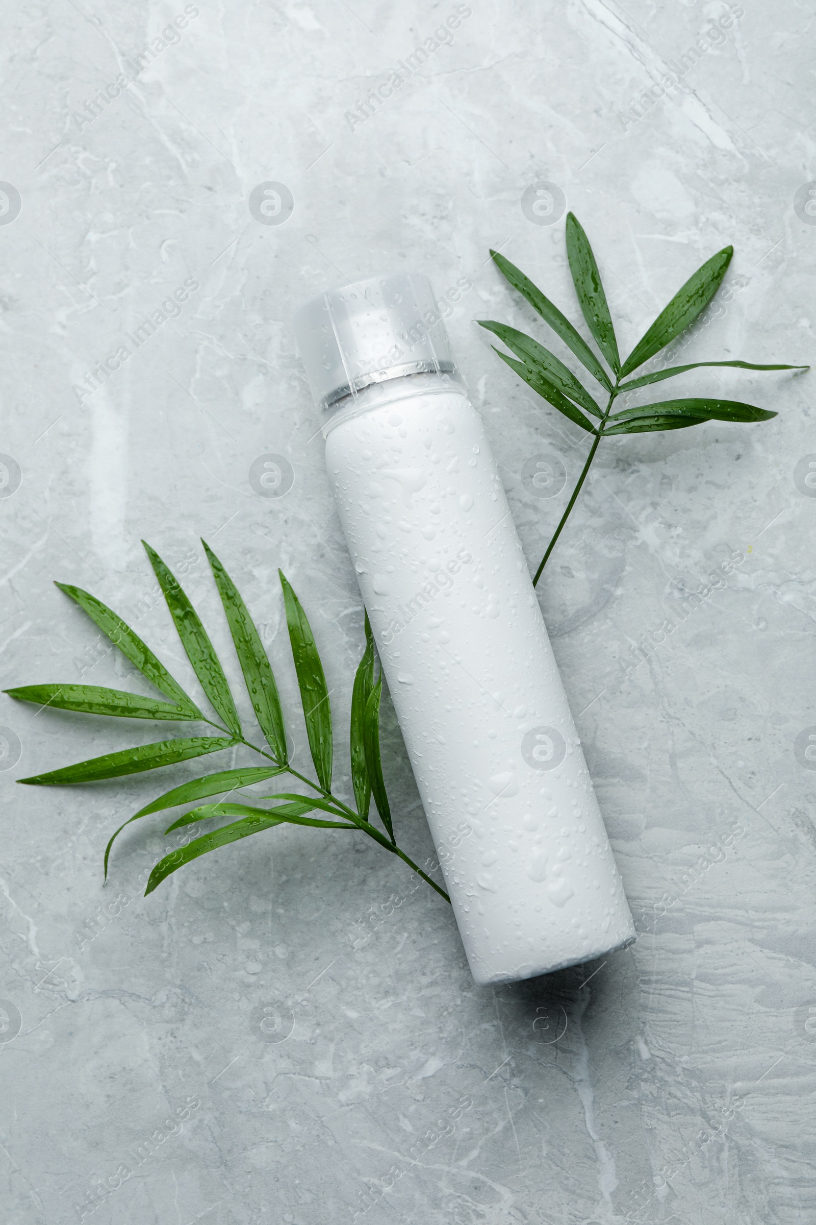 Photo of Dry shampoo spray and green leaves on light grey table, flat lay