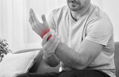 Man suffering from pain in wrist indoors, closeup. Black and white effect