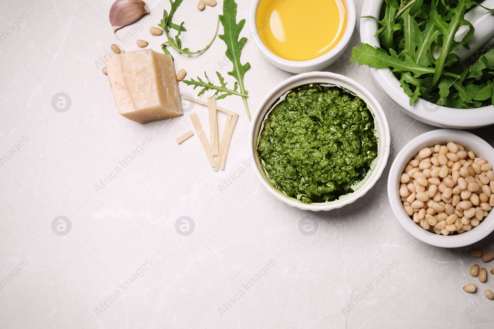 Photo of Bowl of tasty arugula pesto and ingredients on light table, flat lay. Space for text