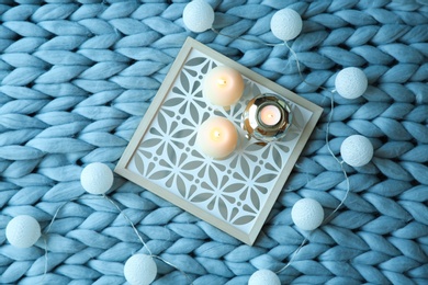 Burning candles and decor on knitted plaid, top view