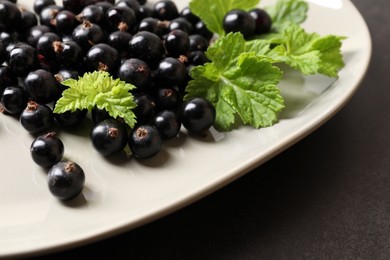 Photo of Plate with ripe blackcurrants and leaves on dark background, closeup