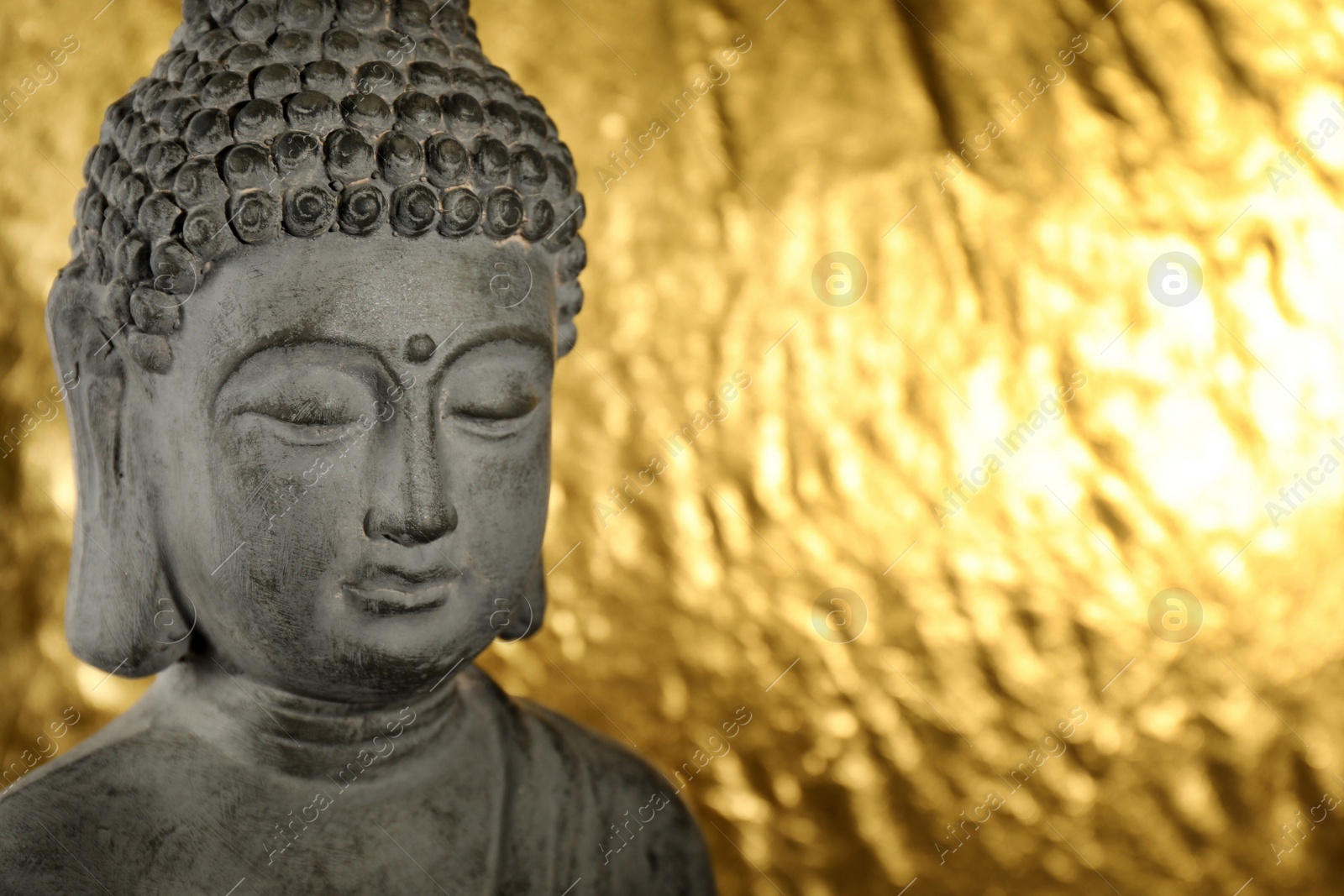 Photo of Buddha statue on golden background, closeup. Space for text