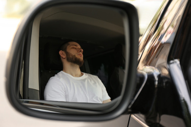 Tired man sleeping in his auto, view through car side mirror