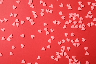 Photo of Bright heart shaped sprinkles on red background, flat lay