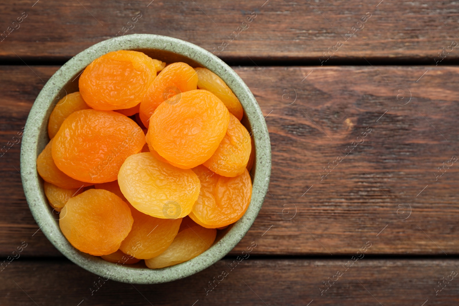 Photo of Bowl of tasty apricots on wooden table, top view and space for text. Dried fruits