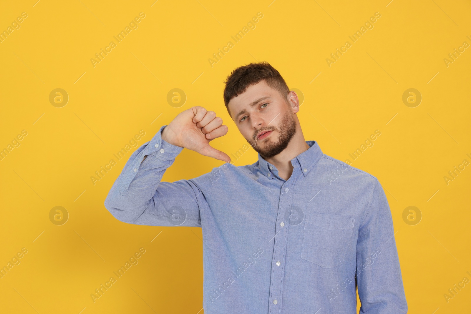 Photo of Young man showing thumb down on orange background