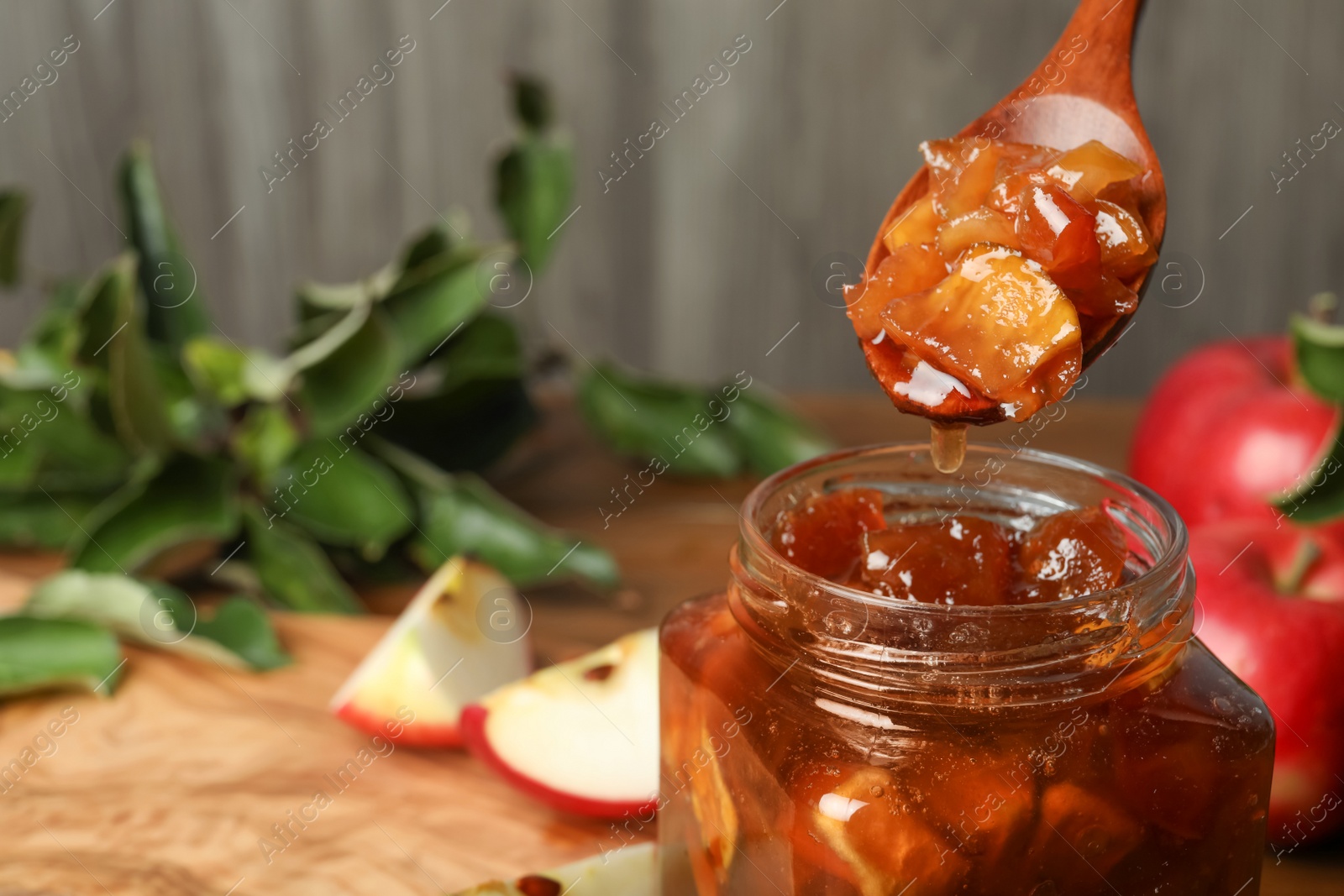 Photo of Spoon with tasty apple jam over glass jar at table, closeup. Space for text