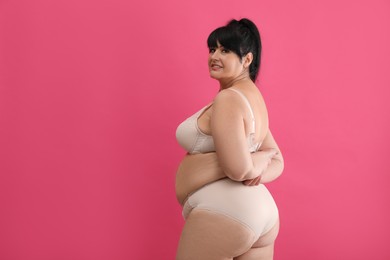 Photo of Beautiful overweight woman in beige underwear on pink background, space for text. Plus-size model