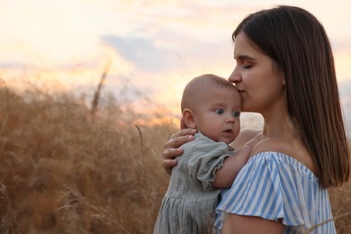 Happy mother with adorable baby in field at sunset, space for text