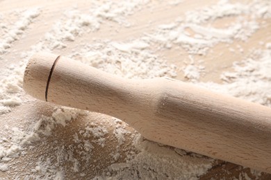 Photo of Scattered flour and rolling pin on wooden table, closeup