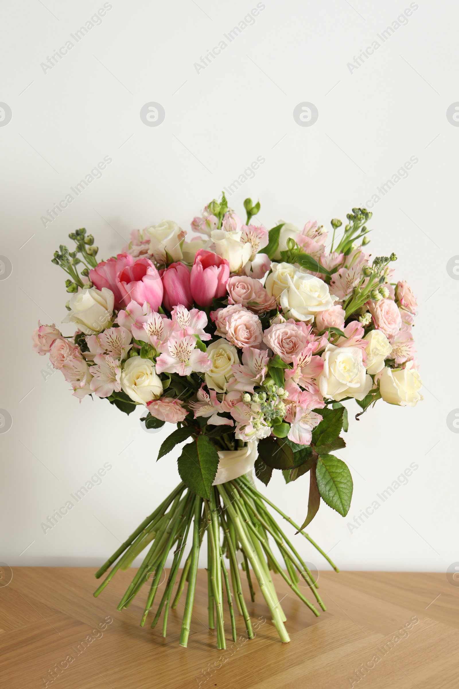 Photo of Beautiful bouquet of fresh flowers on wooden table near white wall