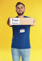 Photo of Male courier holding parcel with sticker Free Delivery on yellow background