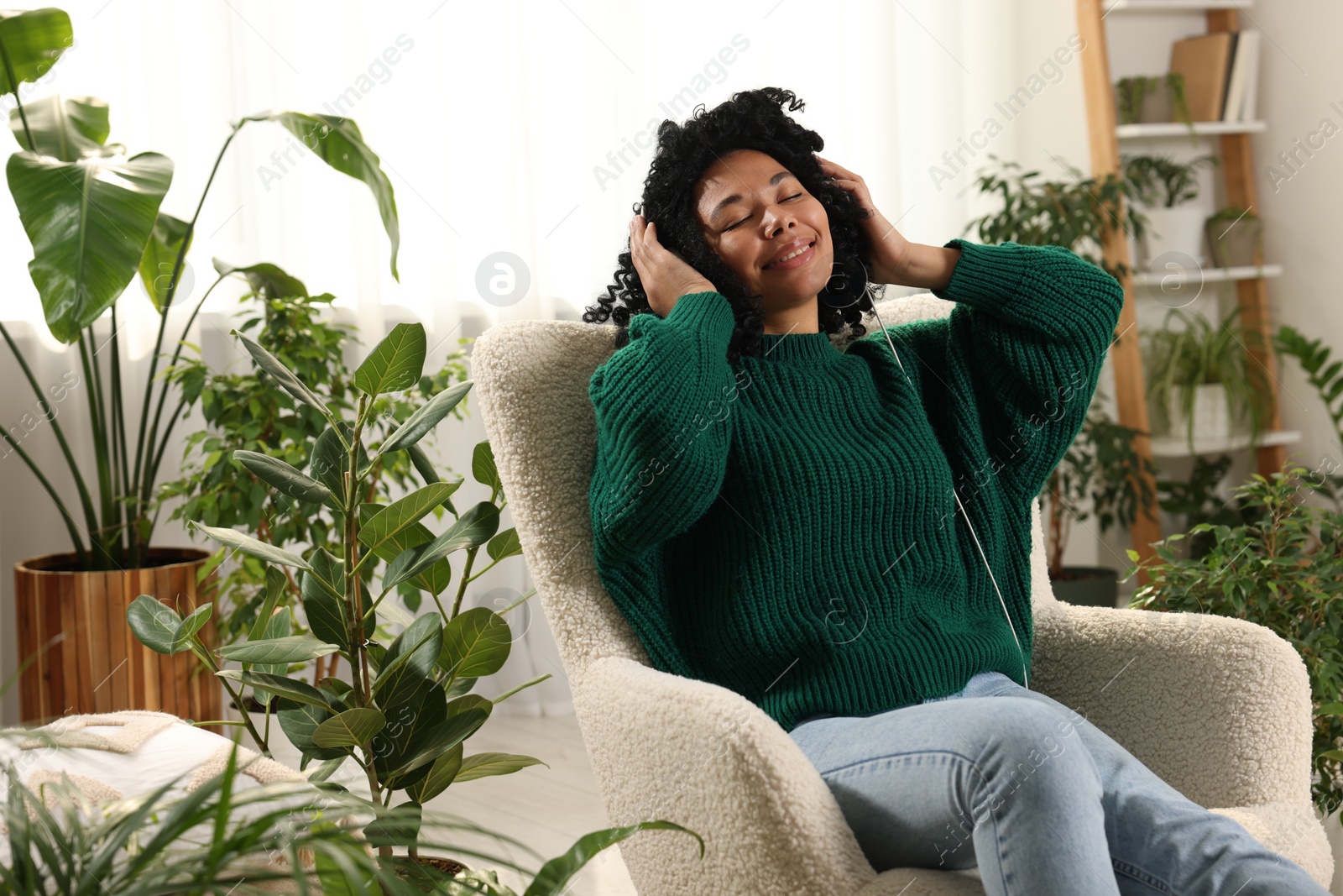Photo of Relaxing atmosphere. Happy woman in headphones listening music surrounded by beautiful houseplants at home