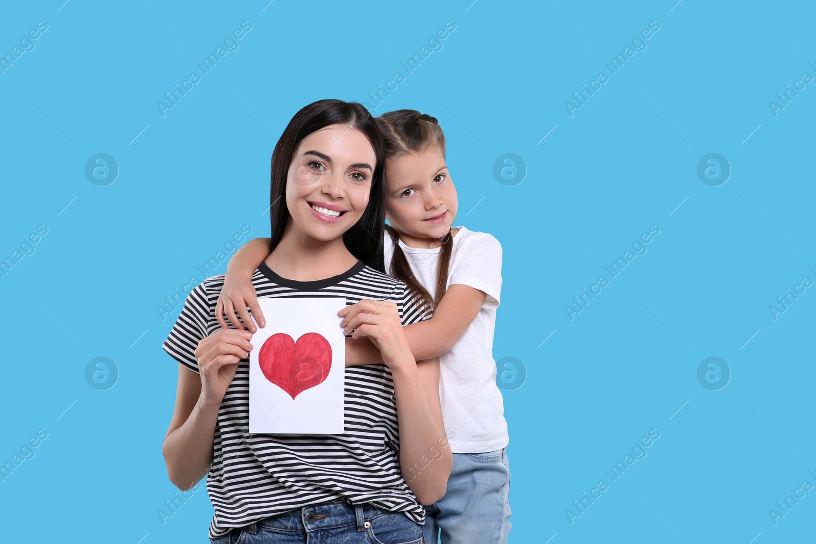 Photo of Happy woman with her cute daughter and handmade greeting card on light blue background, space for text. Mother's day celebration