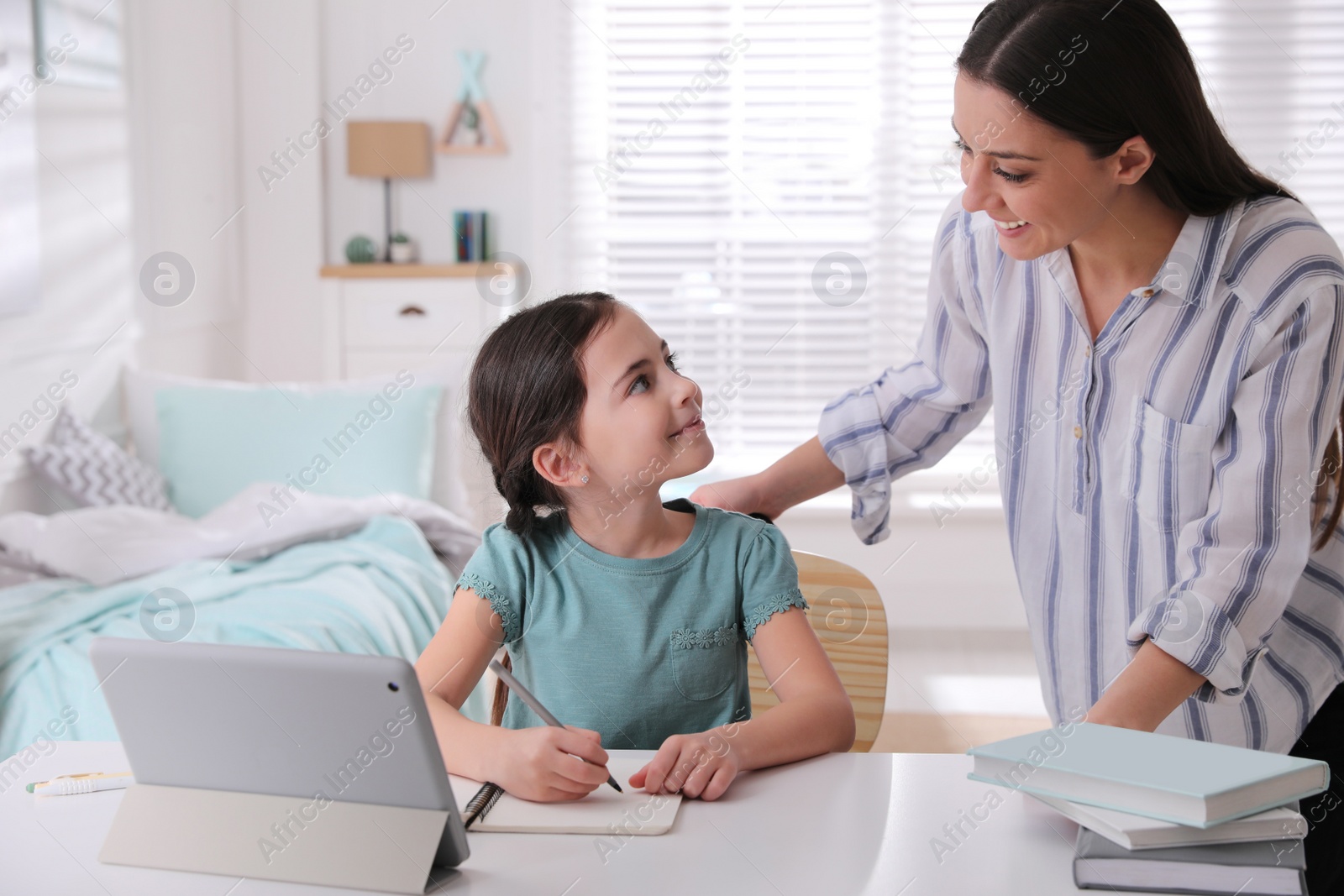 Photo of Mother helping her daughter doing homework with tablet at home