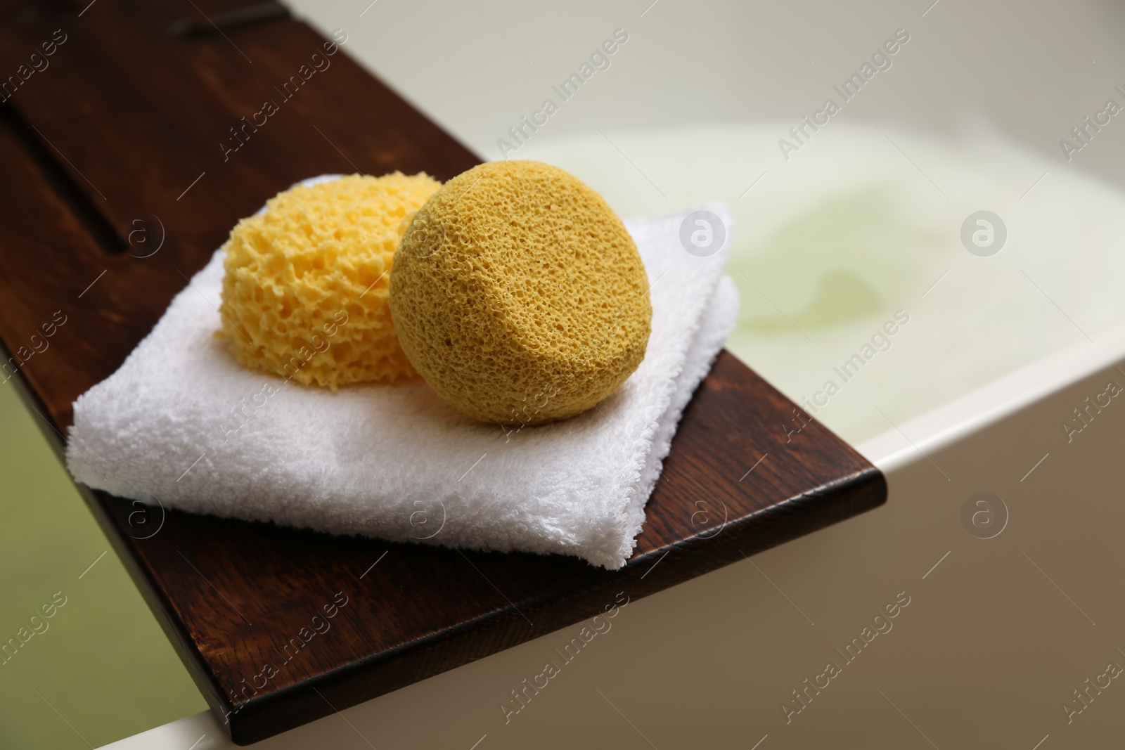 Photo of Wooden bath tray with sponges and towel on tub